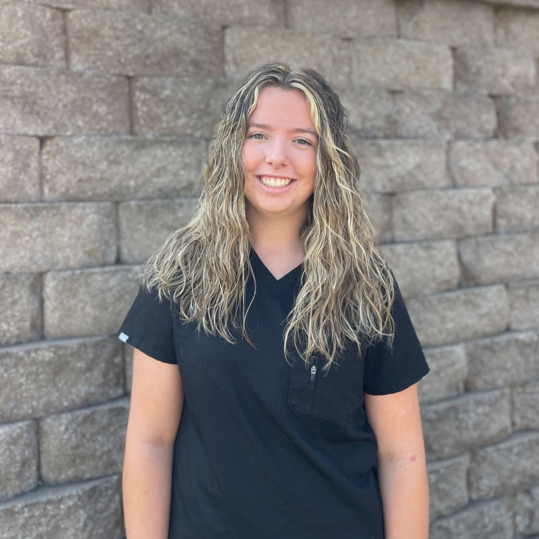 young female veterinary technician assistant smiling in front of brick wall